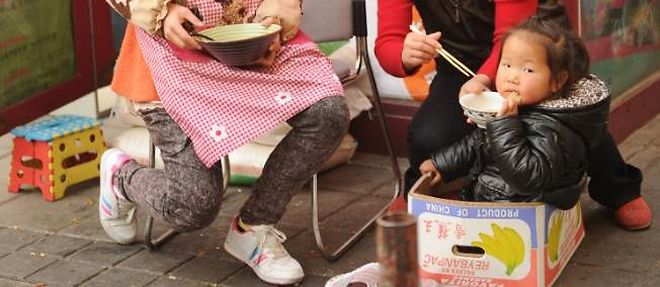 Photo d'illustration : une petite fille nourrie a l'aide de baguettes dans les rues de Shanghai.