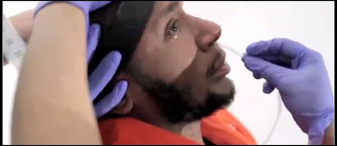 Capture d'ecran d'un extrait de la video montrant le rappeur Mos Def se soumettant a l'alimentation forcee imposee a des detenues de Guantanamo en greve de la faim.
