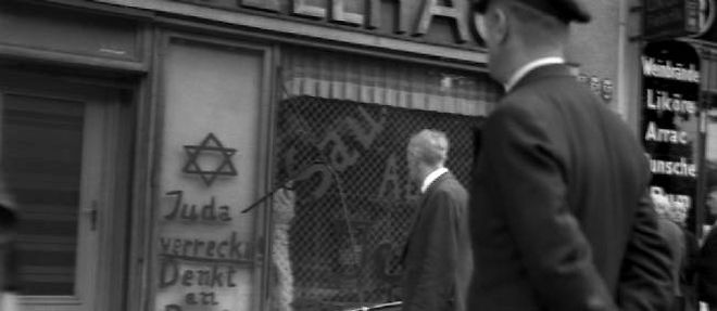 Des passants devant un magasin couvert de slogans antisemites en novembre 1938.