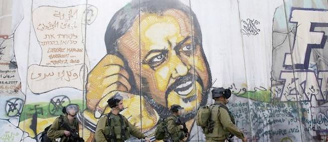 Des soldats israeliens marchent devant le portrait du prisonnier palestinien Marwan Barghouti, dessine sur le mur de separation entre Israel et la Cisjordanie.