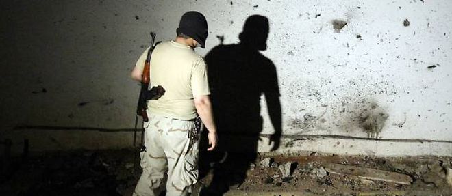Un soldat libyen inspecte les marques d'eclats d'obus sur un mur a Benghazi.
