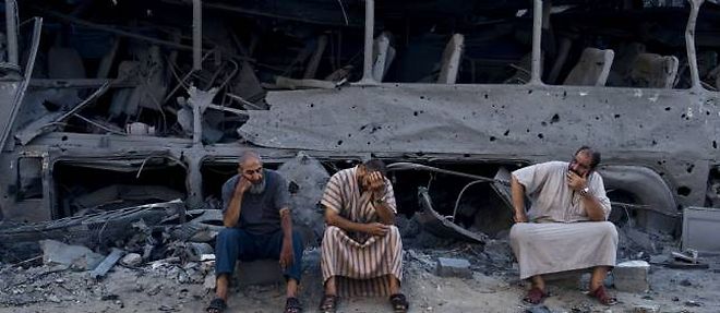 Trois Palestiniens assis devant un bus detruit par une frappe israelienne, mardi 19 aout a Gaza.
