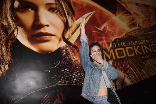 Une etudiante thailandaise fait le salut des rebelles de la sage "Hunger Games" devant l'affiche du film, le 20 novembre 2014 a Bangkok