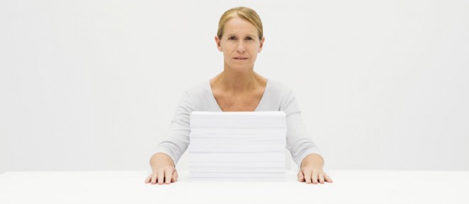Une femme assise derriere une pile de feuilles de papier, photo d'illustration.