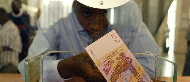 Un homme au guichet d'une banque, on lui tend un billet de 1 000 francs CFA, de la Banque centrale des Etats d'Afrique de l'Ouest (BCEAO).