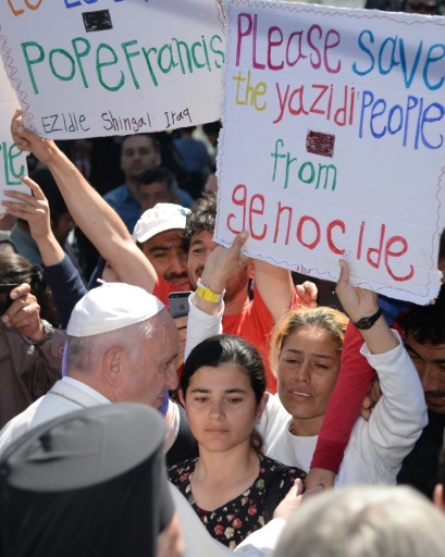 Des femmes brandissent des pancartes appellant à sauver du génocide le peuple Yazidi, lors de la visite du pape François sur l'île de Lesbos, le 16 avril 2016 © FILIPPO MONTEFORTE POOL/AFP