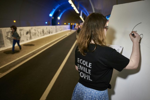 Une femme dessine le long d'une bande-dessinée exposée dans le tunnel de la Croix-Rousse à Lyon le 21 mai 2016 © JEAN-PHILIPPE KSIAZEK AFP