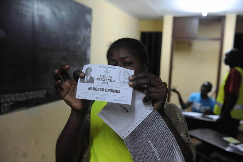 Un membre de la Cenap montre un bulletin d'Ali Bongo Ondimba dans un bureau de vote de Montagne sainte, près de Libreville.  ©  AFP PHOTO / STEVE JORDAN