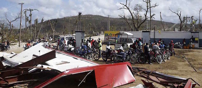 Des Haitiens devant une station-service de Jeremie detruite par l'ouragan Matthew le 10 octobre 2016.