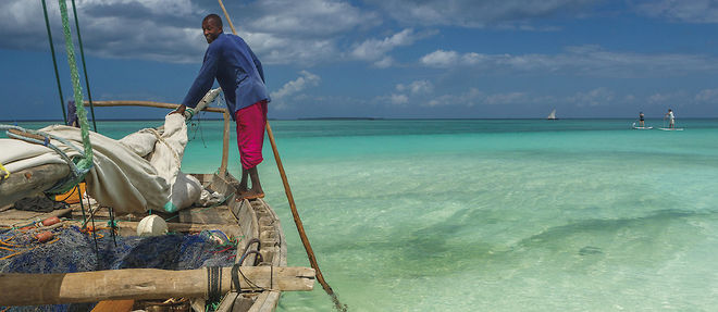 Un pecheur poussant son bateau avec une perche dans des eaux turquoise.