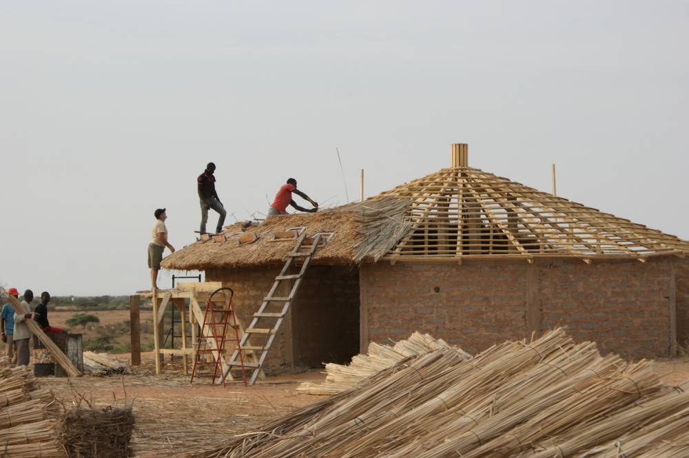 Des hommes en plein travaux d'une maison bâtie avec du typha.  