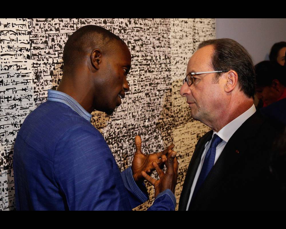 L'artiste sénégalais Babacar Mbaye Diouf explique son oeuvre au président Hollande lors de l'inauguration de l'exposition "Trésors de l'islam en Afrique, de Tombouctou à Zanzibar" le 13 avril 2017 à l'IMA à Paris.  ©  GEOFFROY VAN DER HASSELT / POOL / AFP