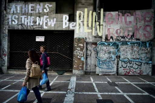 Des personnes marchent devant un graffiti «Athènes est le nouveau Berlin» de l'artiste Cacao Rocks sur le mur d'un ancien bâtiment du centre d'Athènes, le 11 octobre 2017  © LOUISA GOULIAMAKI AFP