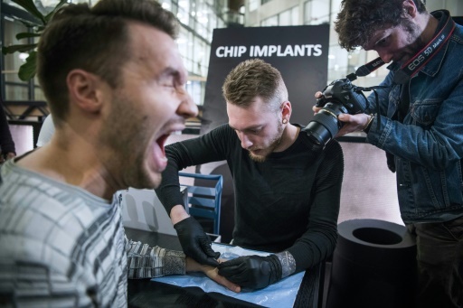 Un homme réagit alors qu'un autre insère un implant sous sa peau, à Stockholm, le 18 janvier 2018 © Jonathan NACKSTRAND AFP