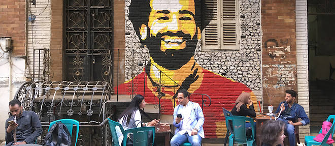 De jeunes Cairotes sont assis &#224; un caf&#233; avec, au-dessus d'eux, le portrait de l'international de football Mohamed Salah.