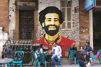  De jeunes Cairotes sont assis à un café avec, au-dessus d'eux, le portrait de l'international de football Mohamed Salah. 