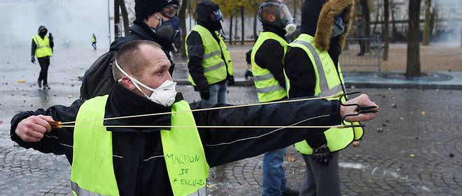 Un manifestant muni d'une fronde visent les forces de l'ordre sur les Champs-Elysees. 