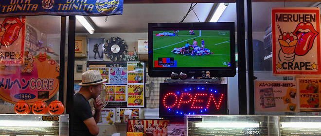 Un commercant regarde un match de rugby dans sa boutique.