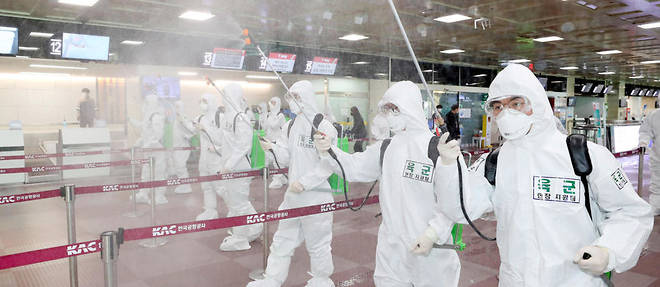 Des militaires sud-coreens equipes de combinaisons de protection repandent du desinfectant dans l'aeroport de Daegu le 6 mars. 
