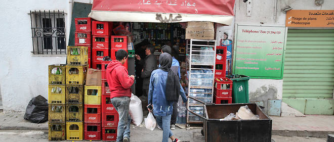 Des Tunisiens attendent leur tour devant un epicier dans la ville d'Ariana, au nord du pays, pour acheter quelques produits alimentaires avant de rentrer chez eux avant le couvre-feu instaure de 18 heures a 6 heures du matin pour ralentir la propagation du coronavirus. 
