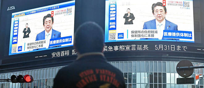 Un homme regarde une declaration du Premier ministre japonais Shinzo Abe sur un ecran geant dans le quartier de Shinjuku a Tokyo.
