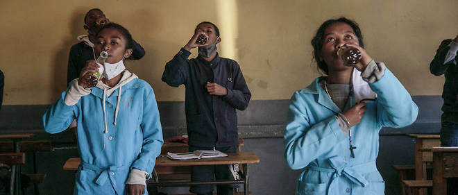 Des eleves brandissent des bouteilles de Covid Organics offertes par les autorites avant le debut des cours au lycee J.-J. Rabearivelo, dans le centre d'Antananarivo, le 23 avril 2020. 
