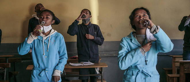 Des eleves brandissent des bouteilles de Covid Organics offertes par les autorites avant le debut des cours au lycee J.-J. Rabearivelo, dans le centre d'Antananarivo, le 23 avril 2020. 
