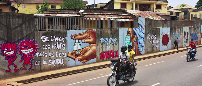 Des motocyclistes passent devant des fresques illustrant les mesures d'hygiene destinees a freiner la propagation de l'epidemie de Covid-19 a Conakry, en Guinee., le 4 mai 2020. 
