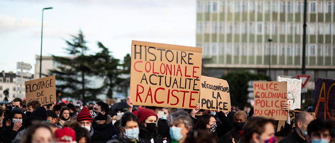 Manifestation contre le projet de loi de securite globale a Nantes, le 5 decembre 2020. Une femme brandit une pancarte sur laquelle est inscrit << histoire coloniale, actualite raciste >>.
