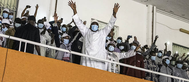 En boubou blanc, du haut d'une tribune, devant ses partisans, dimanche soir, le president reelu Adama Barrow a le sourire et le poing leve en signe de victoire.
