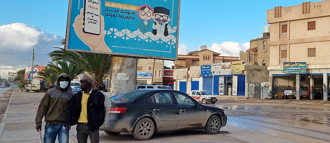 Des travailleurs passent devant un panneau d'affichage electoral indiquant en arabe << Inscrivez-vous et votez avant de rater votre chance >> a Tripoli, la capitale libyenne, le 14 decembre 2021. 
