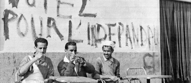 Des Algeriens prennent leur cafe sous une inscription appelant a voter pour l'independance a Alger le 17 juin 1962.
