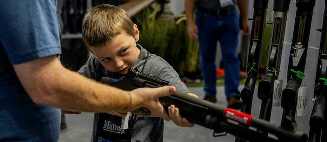 Pendant la convention de la NRA, le 28 mai 2022, un homme aide son fils a epauler une arme a feu.

