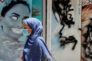  Une Afghane passe devant un salon de beauté affichant des images de femmes qui ont été taguées par crainte des représailles, dans le quartier de Shahr-e Naw à Kaboul, le 20 juillet.   ©Alfred Yaghobzadeh