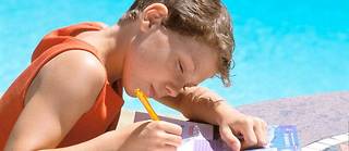 Un enfant travaille sur un cahier de vacances. Image d'illustration.
