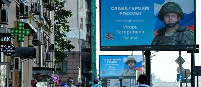 Des habitants de Moscou a l'ete 2022 devant des panneaux "Gloire aux heros de la Russie".
