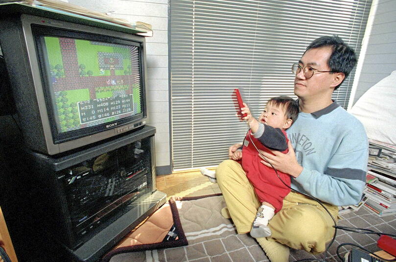 Cette photo d'archive montre Akira Toriyama, en 1988, en train de jouer à<em> Dragon Quest</em>  avec son fils sur les genoux.
 ©  Atsushi Onodera - X07098 - The Yomiuri Shinbum